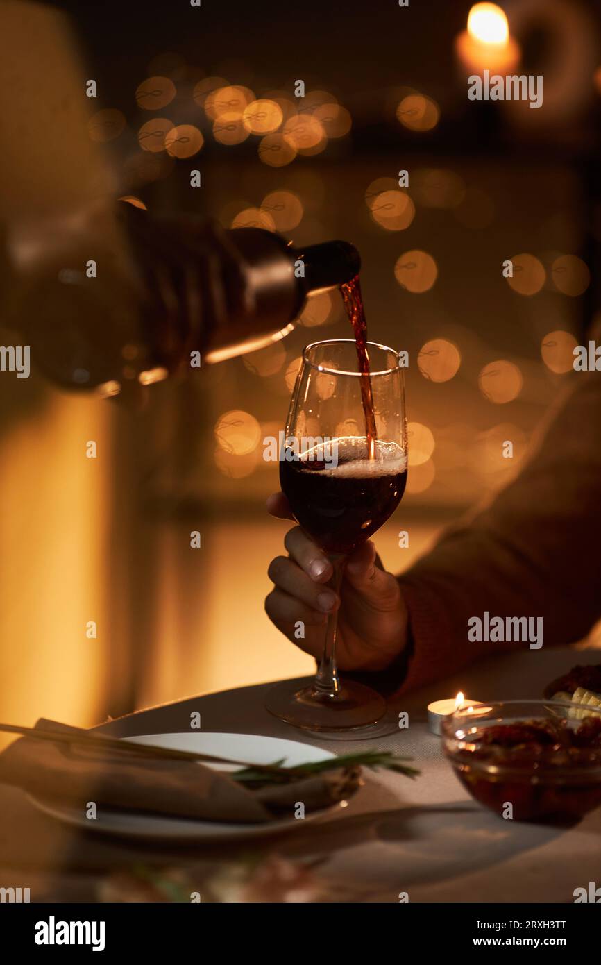 Gros plan d'un couple versant du vin rouge dans un verre pendant un dîner romantique dans l'obscurité Banque D'Images