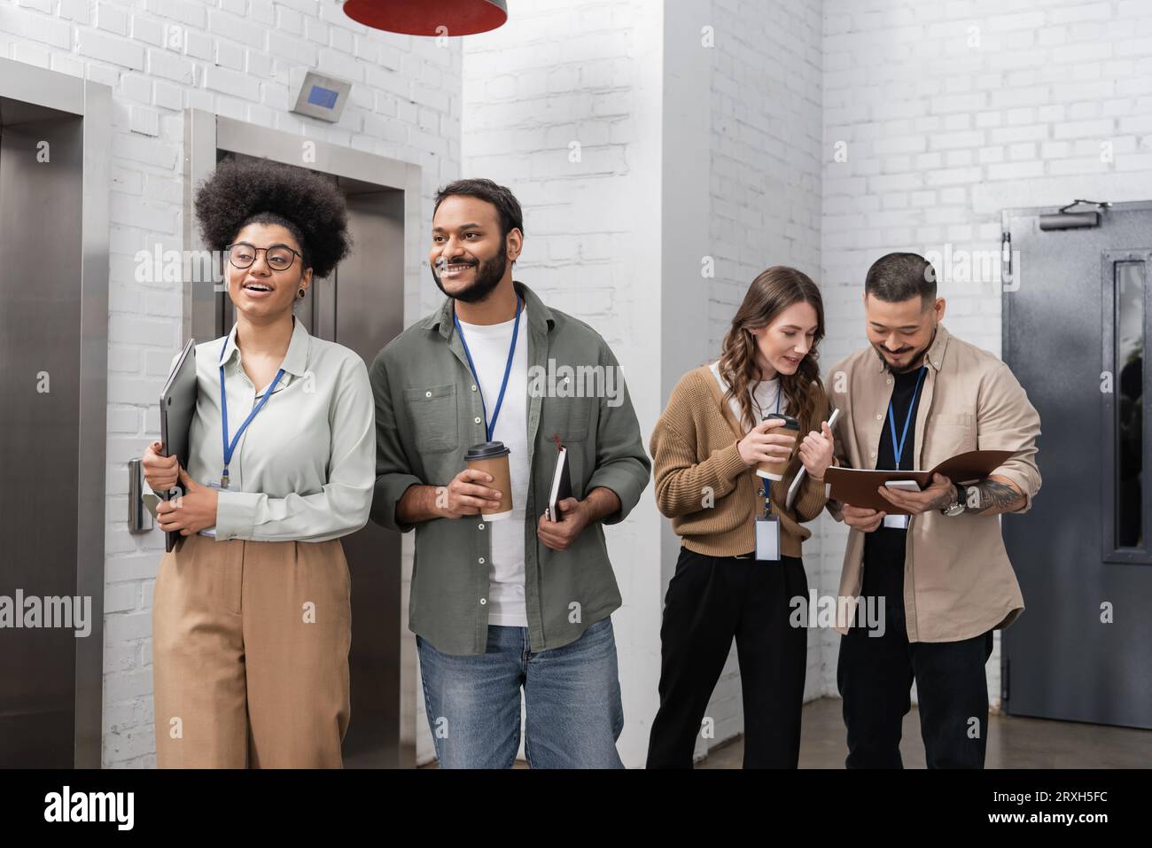 diversité culturelle, heureuse équipe de startup multiculturelle avec badges bavardant près des ascenseurs de bureau Banque D'Images