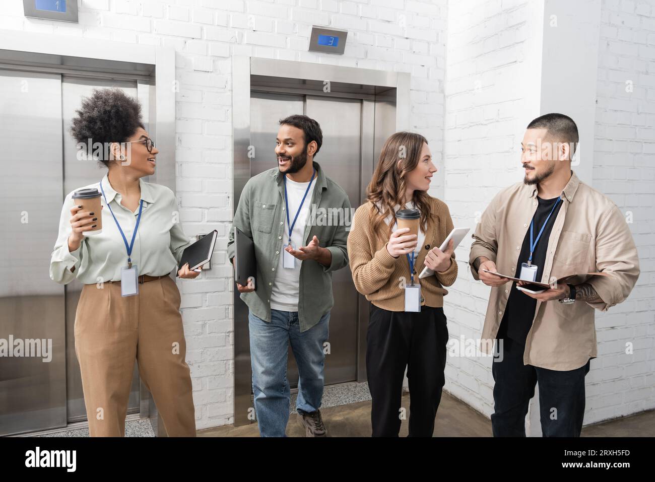 diversité culturelle, équipe créative multiculturelle heureuse avec badges bavardant près des ascenseurs de bureau Banque D'Images