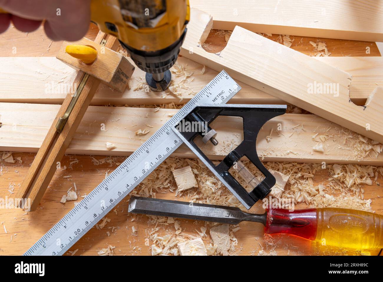 Une personne utilisant une perceuse sur un morceau de bois et d'autres outils de menuiserie sur un établi. Banque D'Images