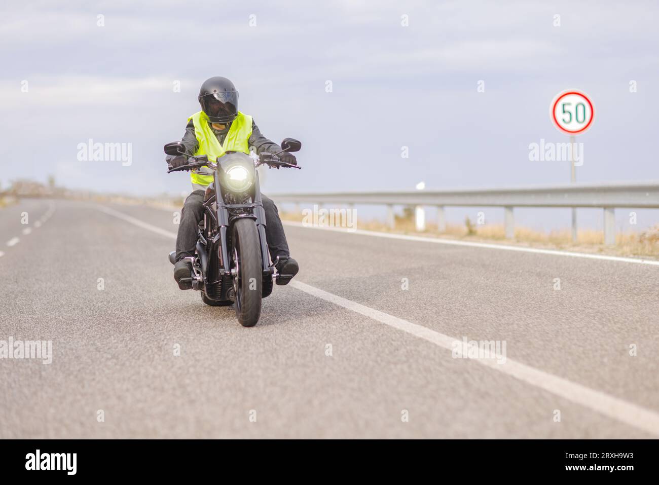 Homme avec un gilet de sécurité réfléchissant conduisant une moto hacheur sur une route ouverte à côté d'un panneau de signalisation de limite de vitesse Banque D'Images