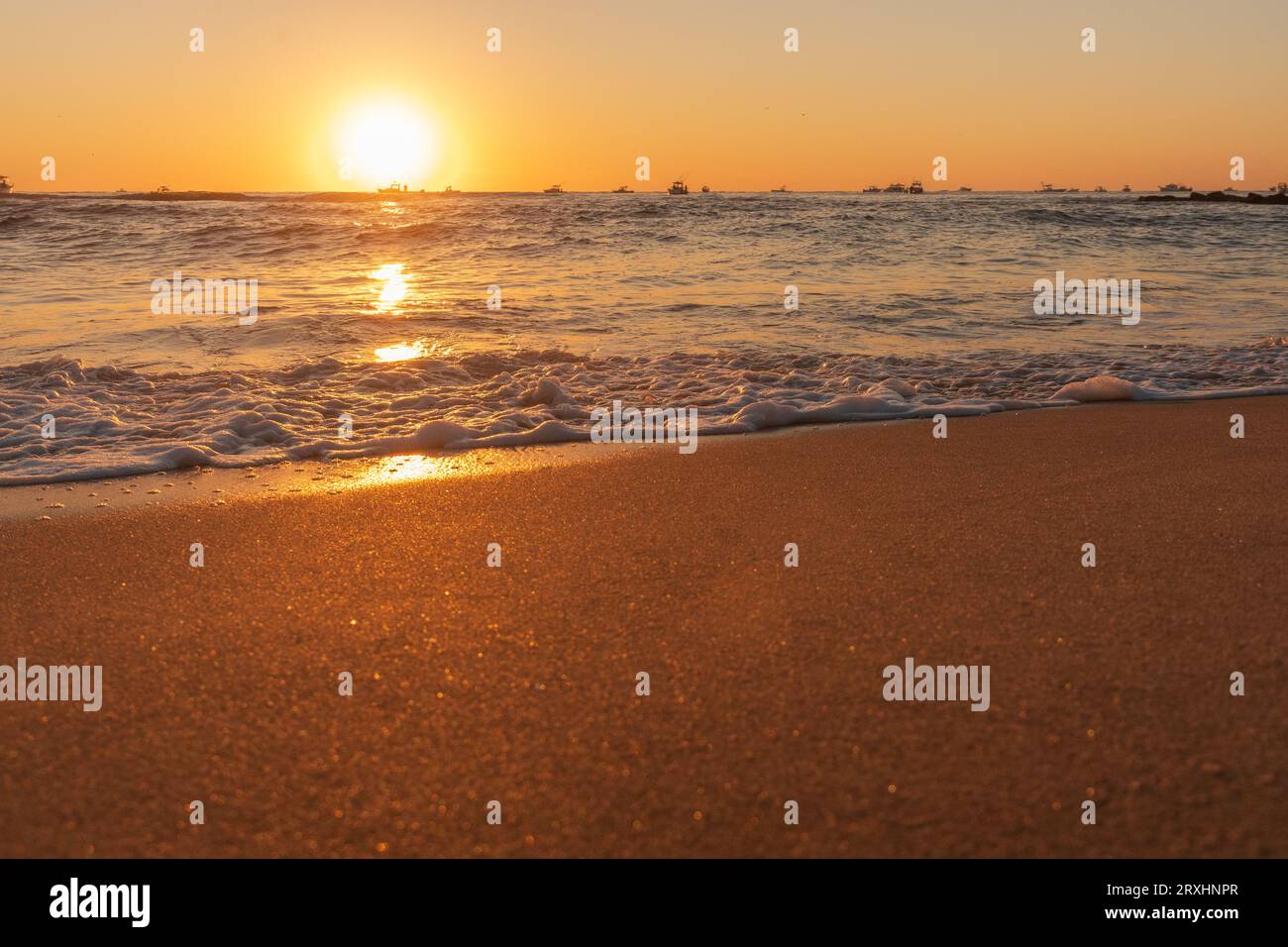 Lever du soleil et surfer sur le rivage du New Jersey avec des bateaux de pêche en arrière-plan Banque D'Images