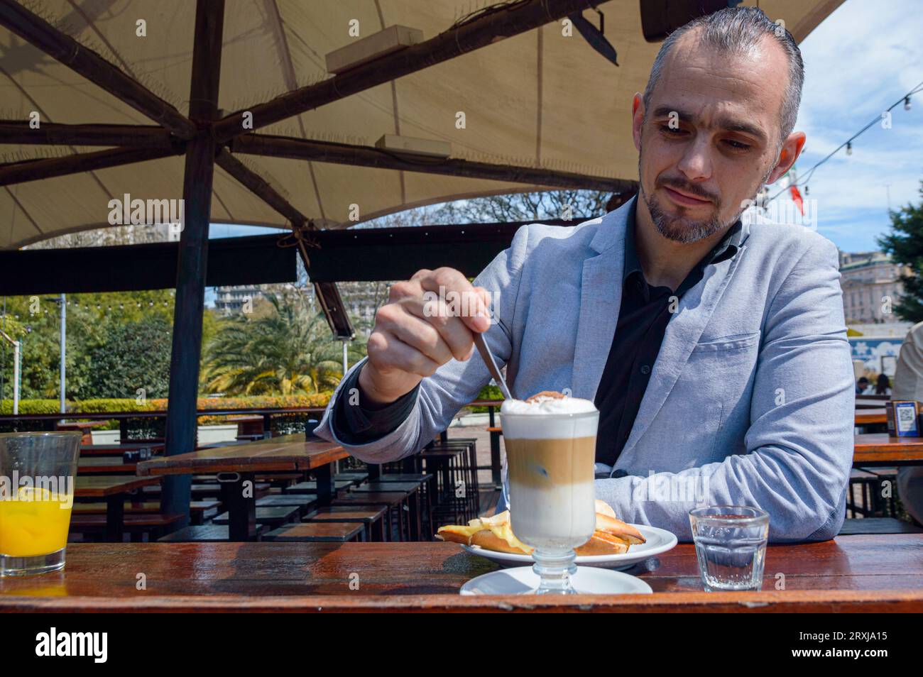 Homme adulte français caucasien avec barbe, souriant heureux d'avoir le petit déjeuner de café avec sandwich et jus d'orange assis à l'extérieur du restaurant, de la nourriture et dr Banque D'Images