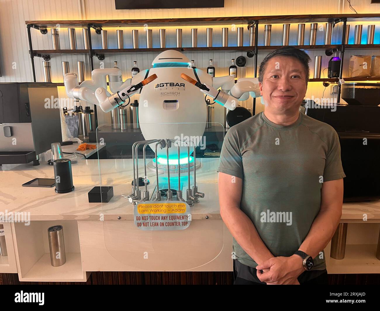 New York, États-Unis. 18 août 2023. Sunny Lam, fondateur du Botbar Cafe dans le quartier Greenpoint de Brooklyn, se trouve à côté du barista Adam et est la première machine à café robot de la métropole de la côte est des États-Unis. De plus en plus de robots effectuent des tâches simples dans les restaurants. Maintenant New York a son premier robot-barista. (Pour dpa 'Adam fait le café - New York a son premier robot barista') crédit : Benno Schwinghammer/dpa/Alamy Live News Banque D'Images