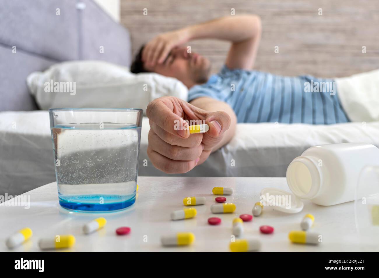 jeune homme prenant la pilule de médicament pour la gueule de bois dans le lit à la maison, souffrant de maux de tête, migraine. un homme souffre d'un mal de tête pendant un rhume en mentant Banque D'Images