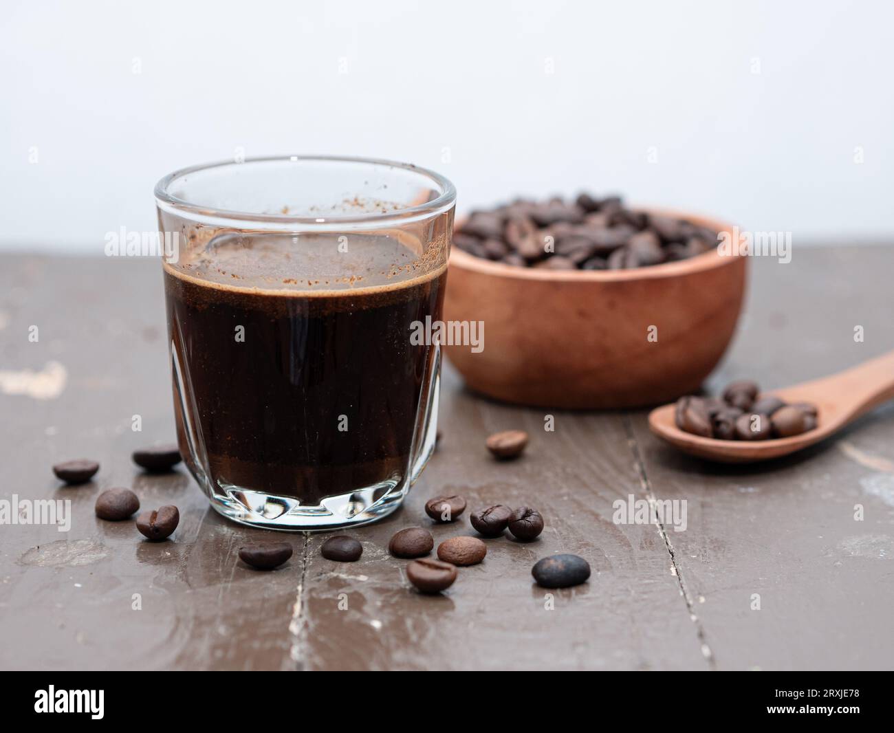 Café expresso noir dans une tasse en verre avec des grains de café sur une table en bois Banque D'Images