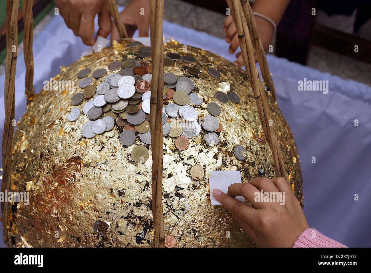 Une photo d'un stupa doré par de jeunes enfants et des personnes âgées, avec le stupa recouvert de feuilles d'or et de nombreuses pièces d'argent placées dessus. Banque D'Images