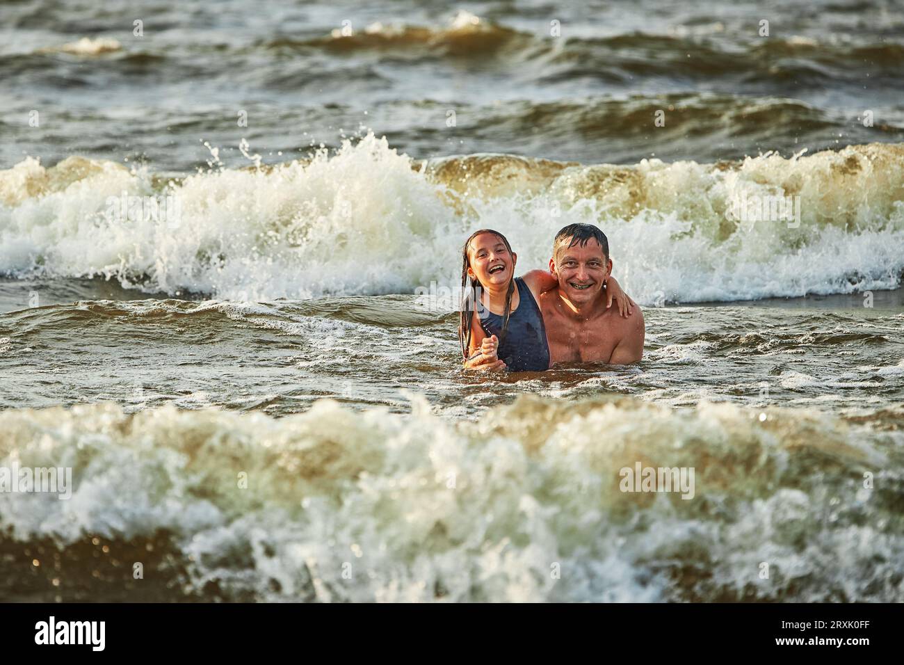 Petite fille et son père jouant avec les vagues dans la mer. Vacances d'été en famille. Gamin éclaboussant de manière ludique avec les vagues avec son père. Sauter en soi Banque D'Images