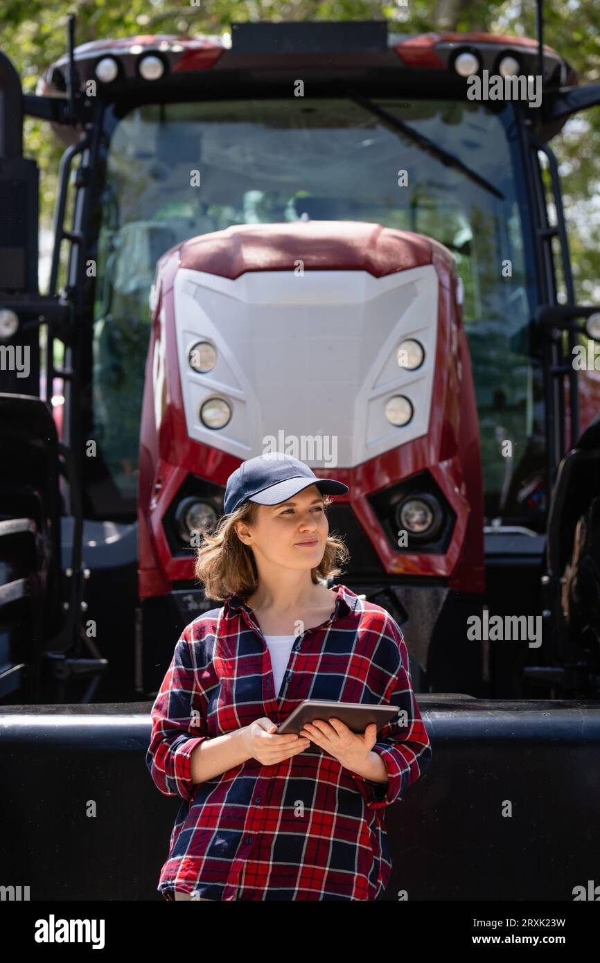 Femme agriculteur avec une tablette numérique sur le fond d'un tracteur agricole. Banque D'Images