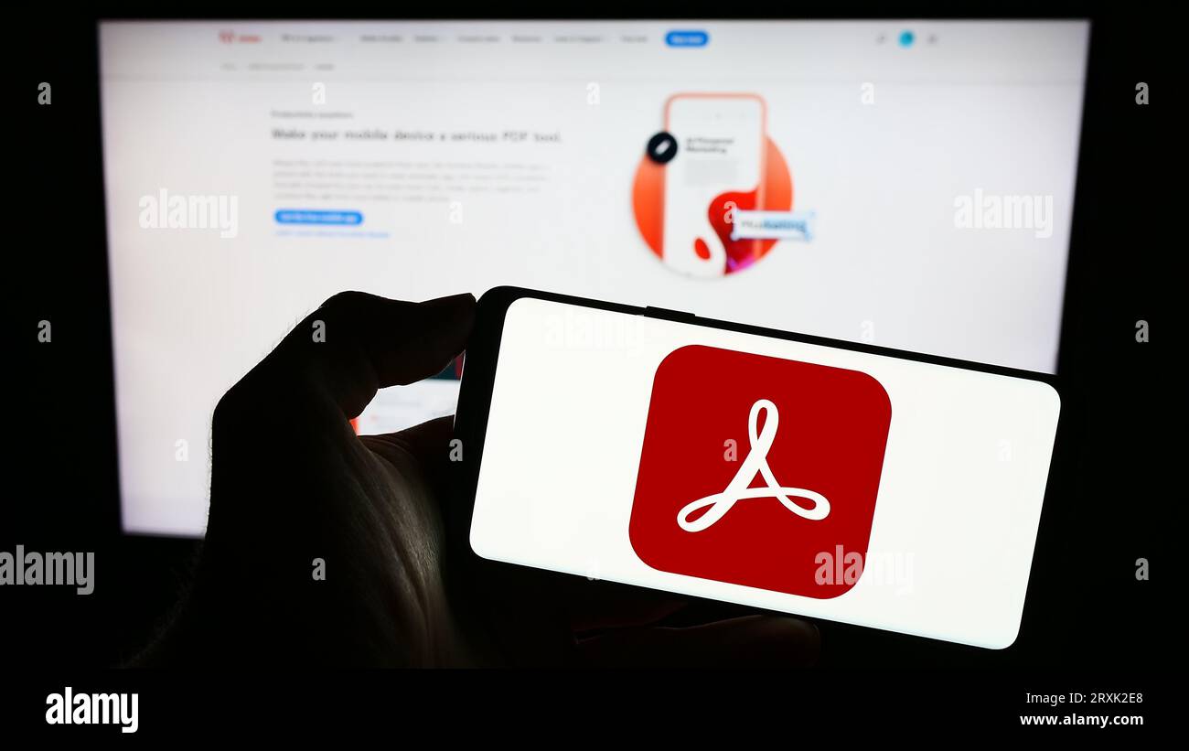 Personne tenant le téléphone cellulaire avec le logo du logiciel de gestion PDF Adobe Acrobat sur l'écran devant la page Web de l'entreprise. Concentrez-vous sur l'affichage du téléphone. Banque D'Images