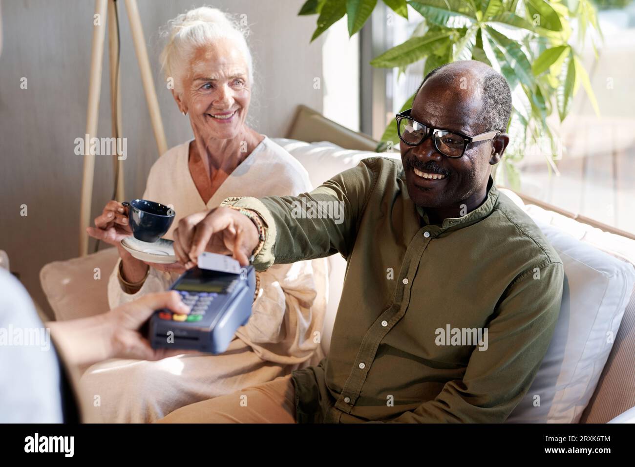 Homme afro-américain souriant payer pour le café avec carte de crédit tout en étant assis dans le café avec sa femme Banque D'Images