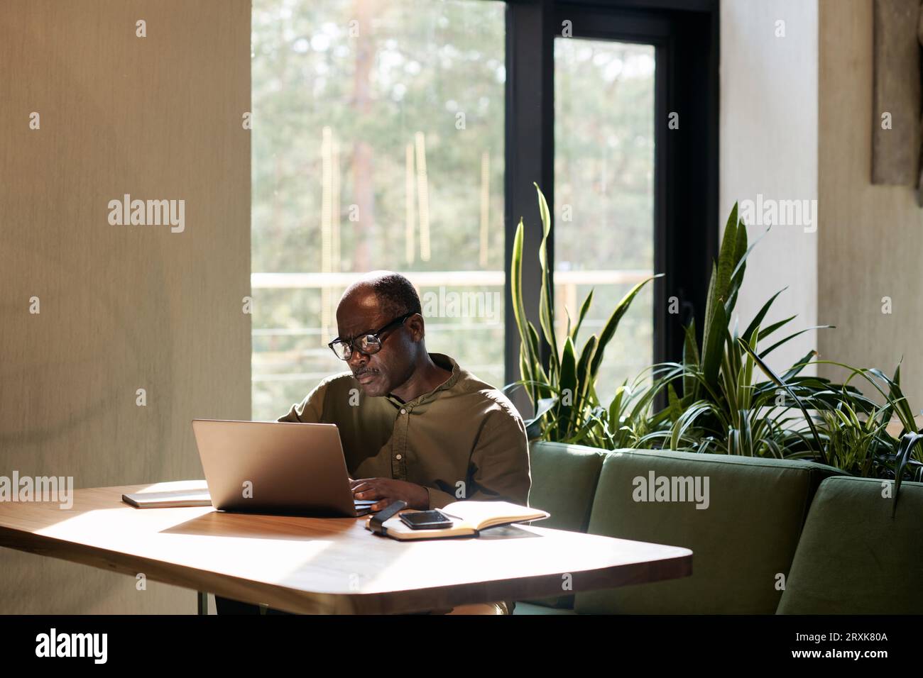 Homme senior afro-américain travaillant sur ordinateur portable assis à table dans un café Banque D'Images
