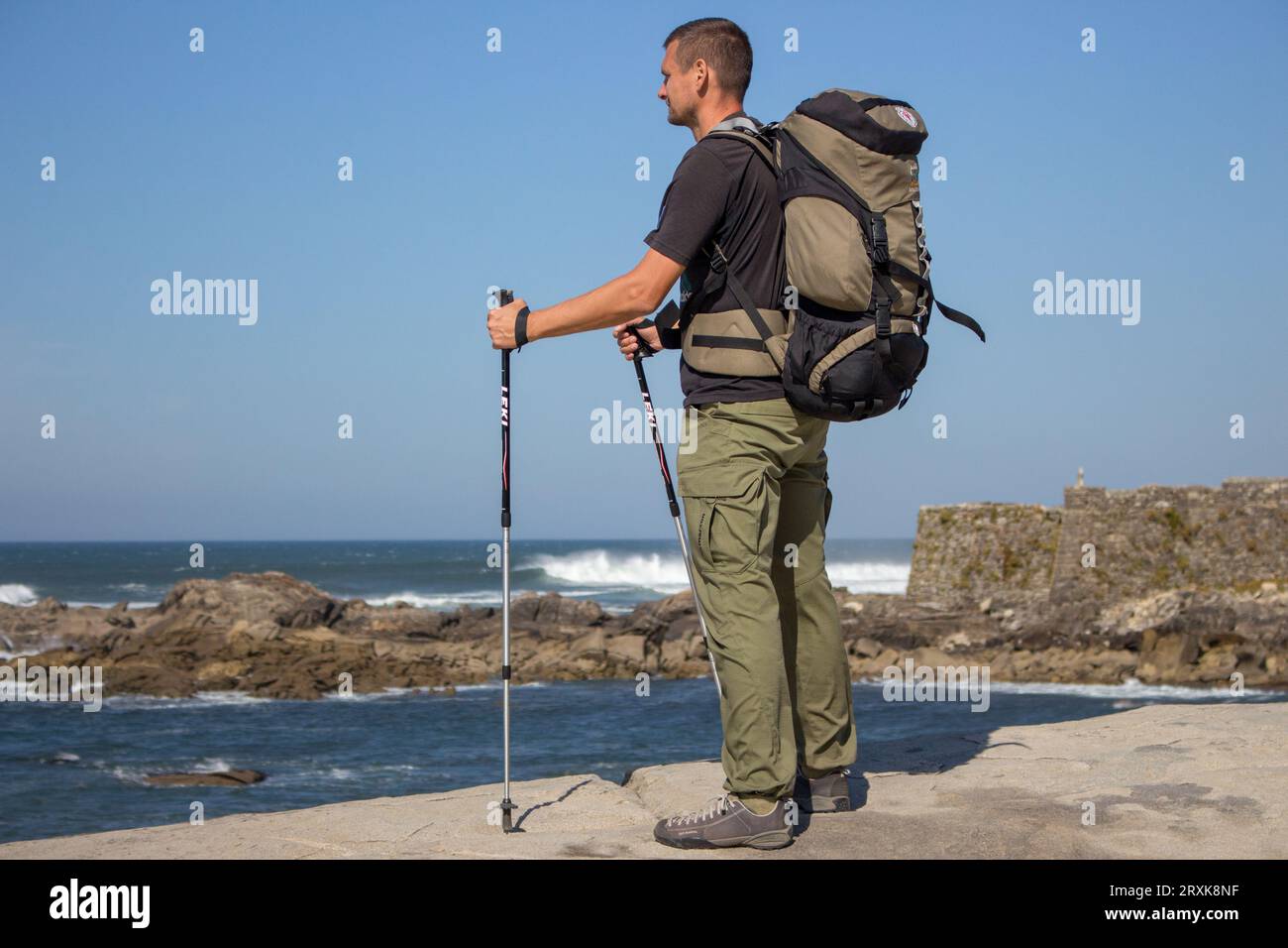 Touriste avec grand sac à dos et bâtons sur la côte de l'océan Atlantique. Pèlerin sur Camino de Santiago, Portugal. Fond de paysage marin pittoresque. Banque D'Images