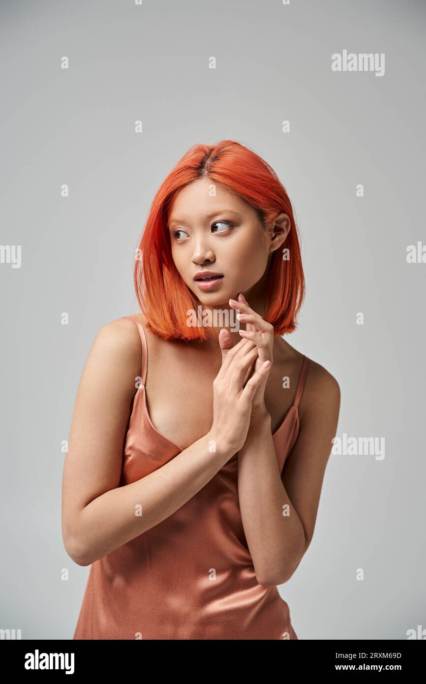 portrait de jeune femme asiatique rêveuse avec les cheveux rouges posant dans la robe de glissement de soie sur fond gris Banque D'Images