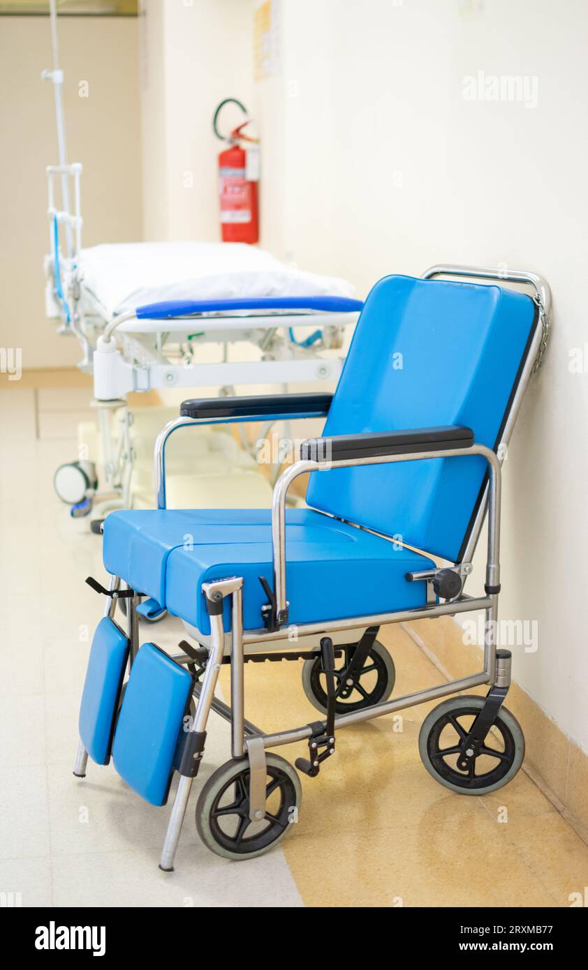 Fauteuil roulant rembourré bleu spécialisé avec civière d'hôpital dans le fond de couloir Banque D'Images