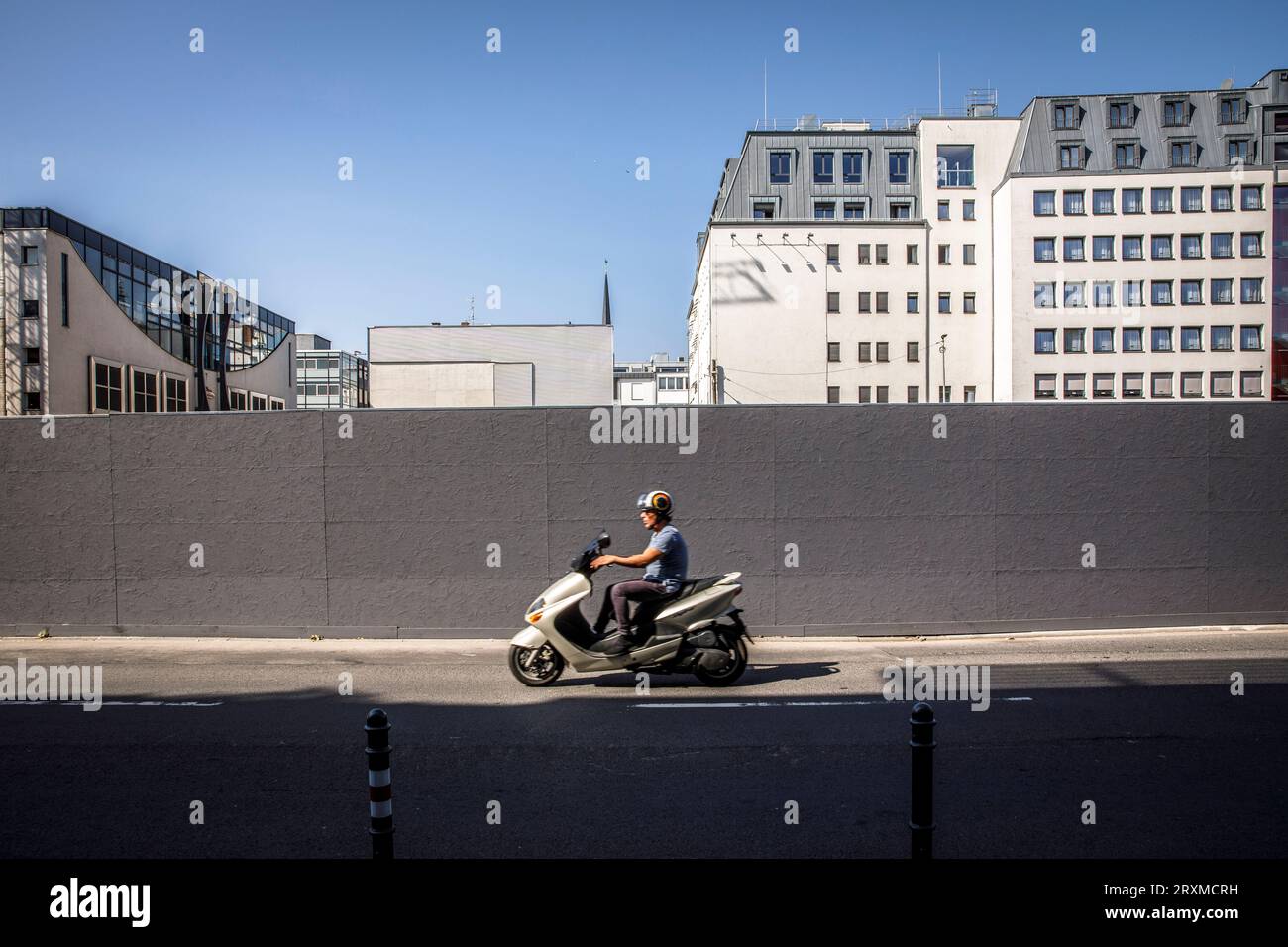 Un conducteur de scooter passe devant une clôture de construction près de la cathédrale, Cologne, Allemagne. ein Motorrollerfahrer faehrt an einem Bauzaun nahe Dom Banque D'Images