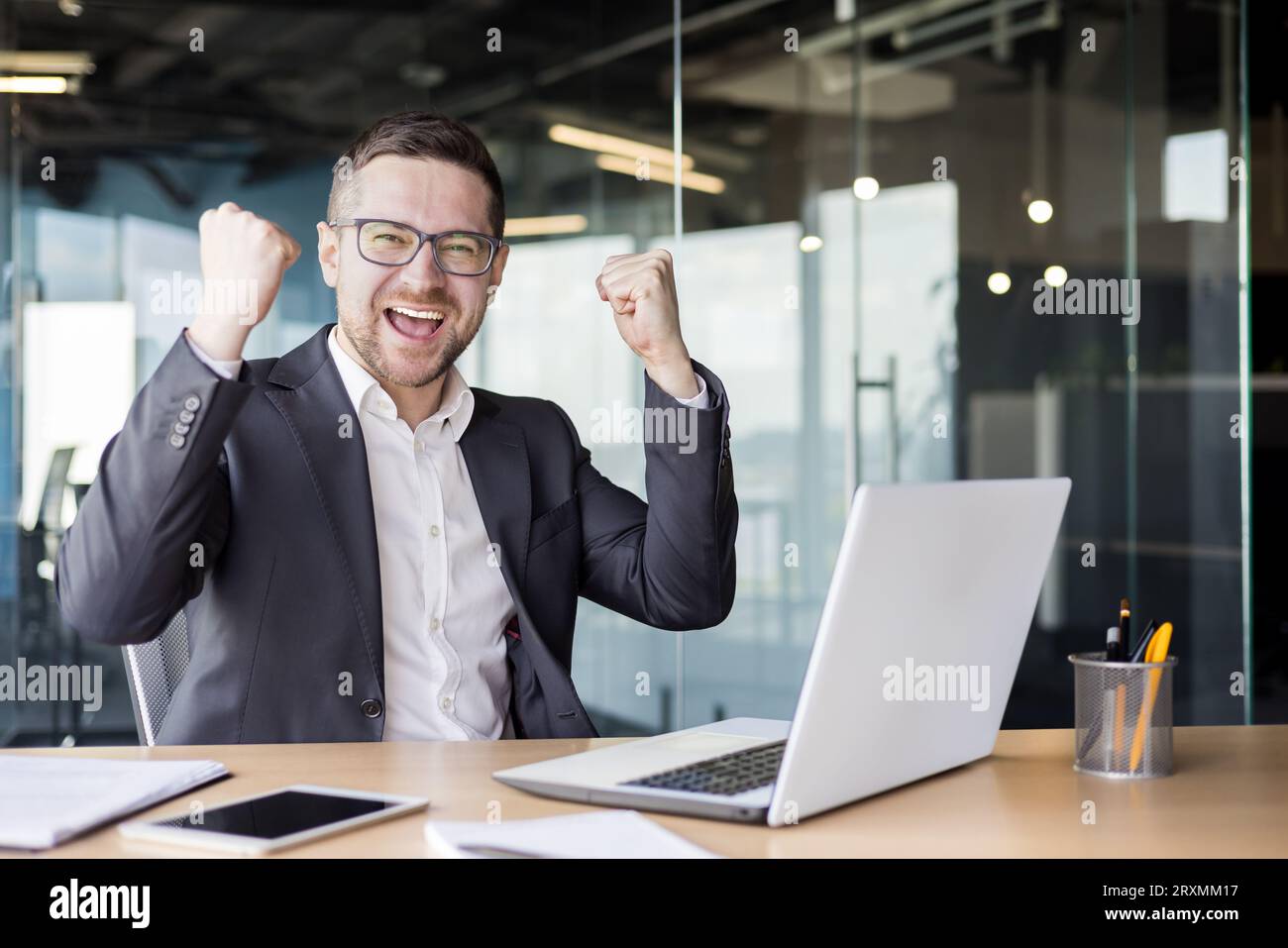 Portrait d'un jeune homme d'affaires heureux assis à un bureau dans le bureau et célébrant le succès au travail. Banque D'Images