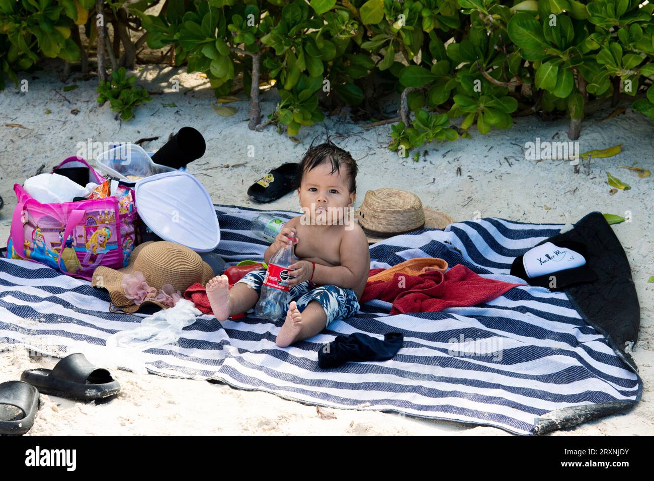 Jeune garçon latino assis sur une couverture de serviette sur une plage de sable blanc à Cancun, au Mexique. Banque D'Images