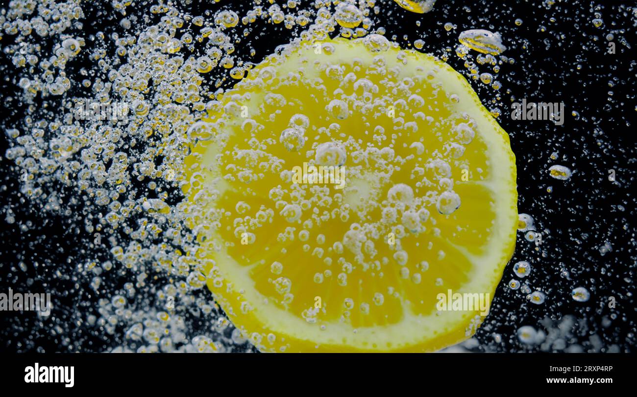 Sous l'eau de limonade sucrée fraîchement pressée que les citrons crus tranchent tombant dans l'eau de soude sur fond bleu foncé ou noir. Gros plan lemonad Banque D'Images