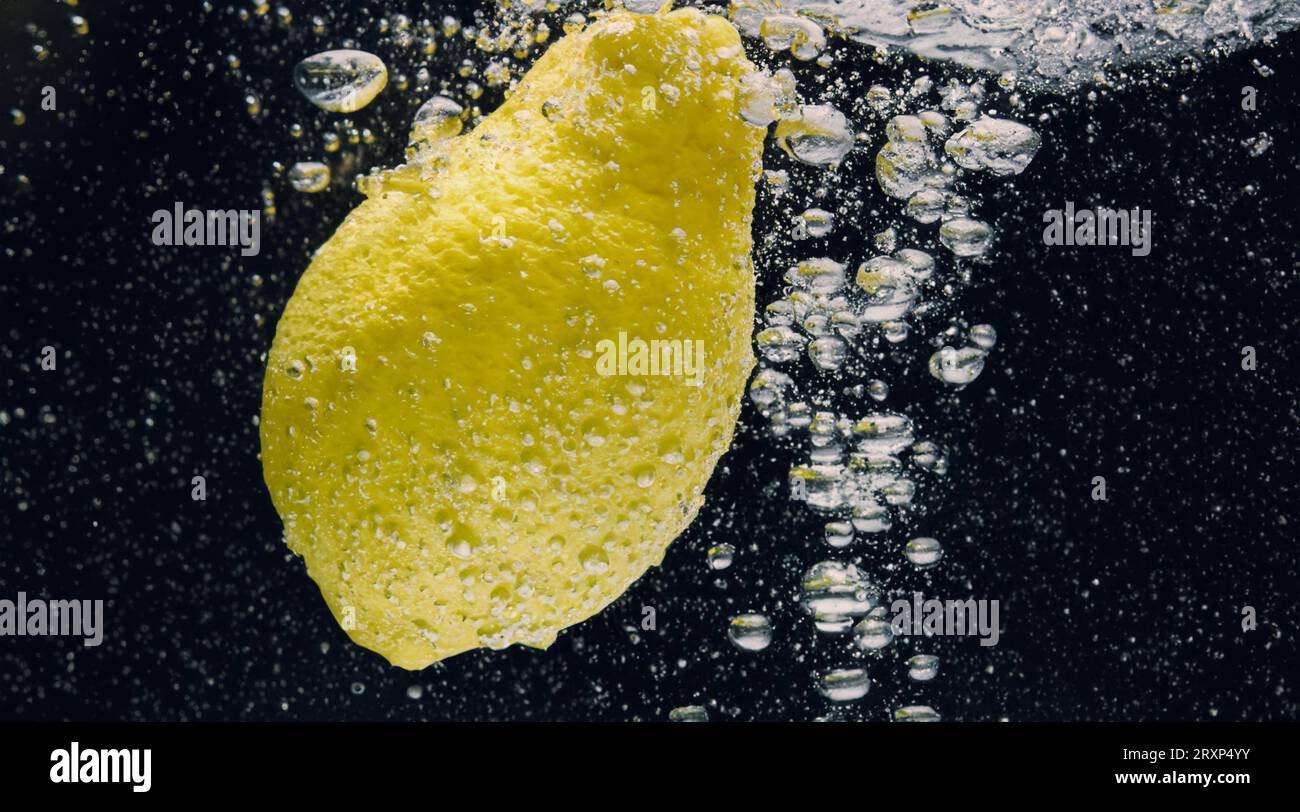 Sous l'eau de limonade sucrée fraîchement pressée que les citrons crus tranchent tombant dans l'eau de soude sur fond bleu foncé ou noir. Gros plan lemonad Banque D'Images