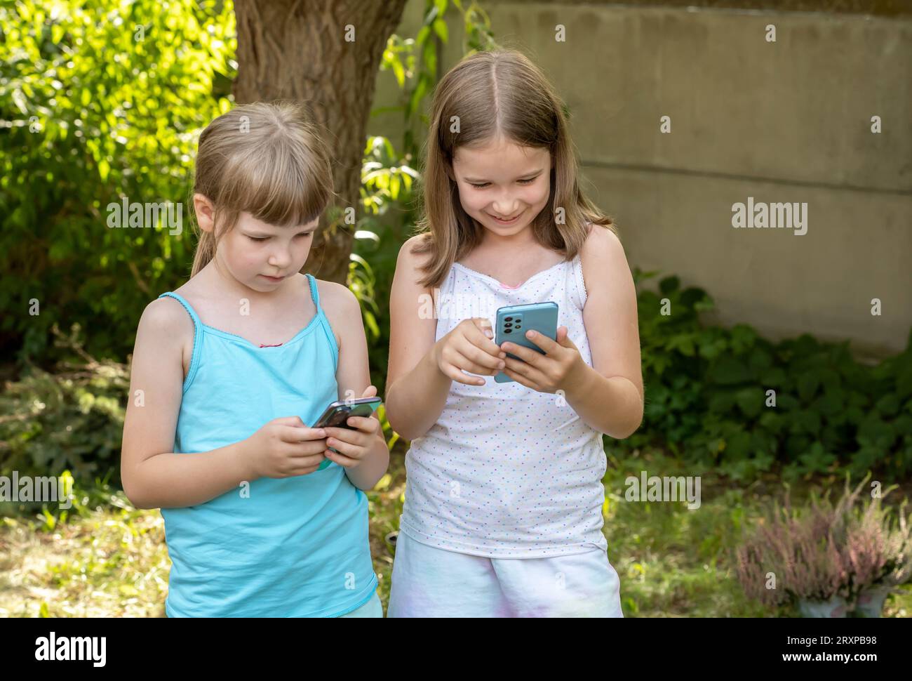 Filles enfants tenant leurs smartphones dans les mains, enfants à l'extérieur regardant leurs téléphones mobiles rire, en utilisant la technologie, les applications, la scène extérieure, réel Banque D'Images