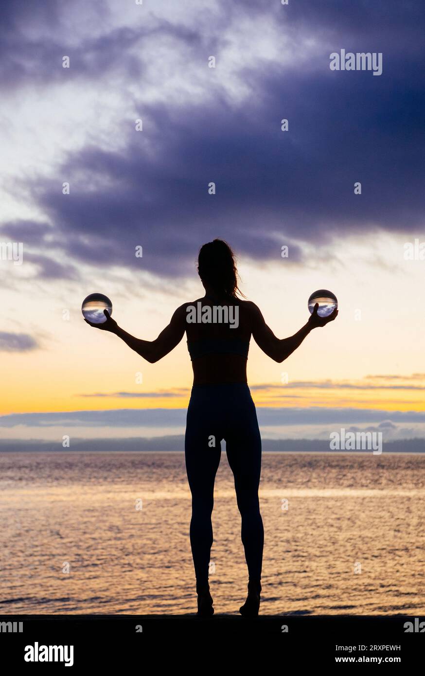 Silhouette de femme s'exerçant avec des haltères sur le dessus du banc côtier au crépuscule nuageux Banque D'Images