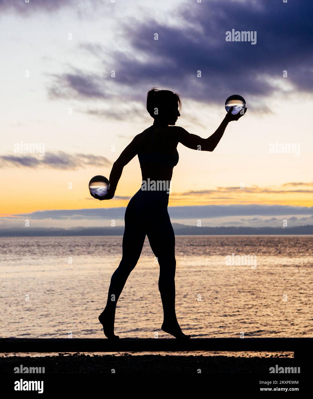 Silhouette de femme s'exerçant avec des haltères sur le dessus du banc côtier au crépuscule nuageux Banque D'Images