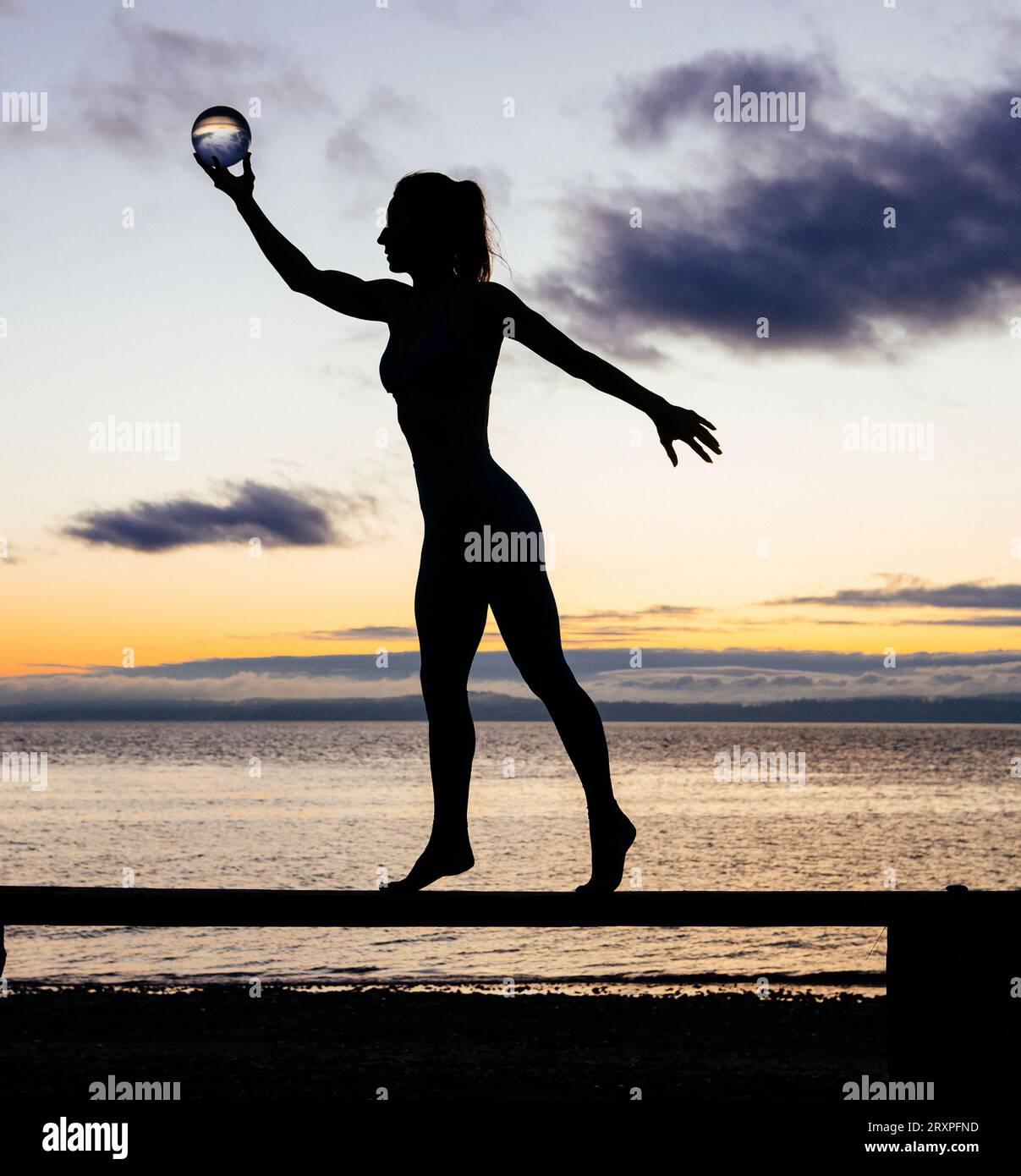 Silhouette de femme s'exerçant avec des haltères sur le dessus du banc côtier au crépuscule nuageux Banque D'Images
