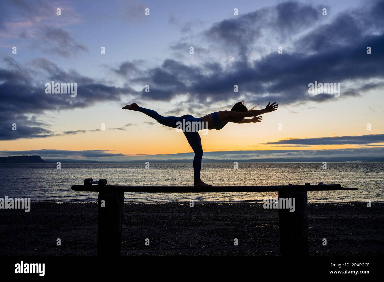 Silhouette de femme s'exerçant avec des haltères sur le dessus du banc côtier au crépuscule nuageux Banque D'Images
