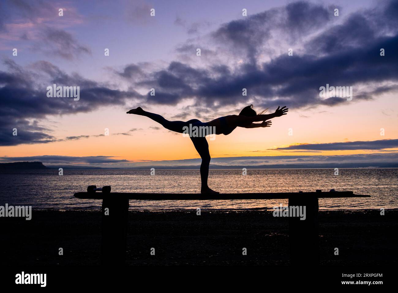 Silhouette de femme s'exerçant avec des haltères sur le dessus du banc côtier au crépuscule nuageux Banque D'Images