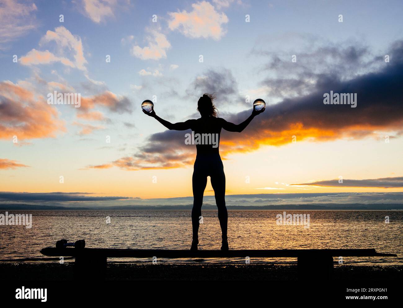 Silhouette de femme s'exerçant avec des haltères sur le dessus du banc côtier au crépuscule nuageux Banque D'Images