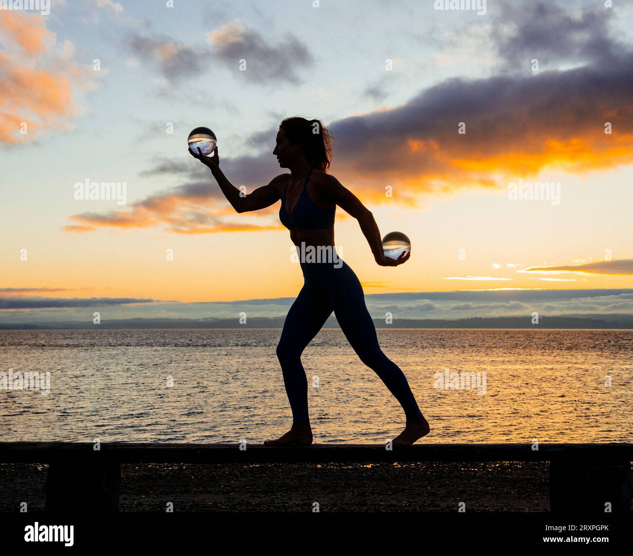Silhouette de femme s'exerçant avec des haltères sur le dessus du banc côtier au crépuscule nuageux Banque D'Images