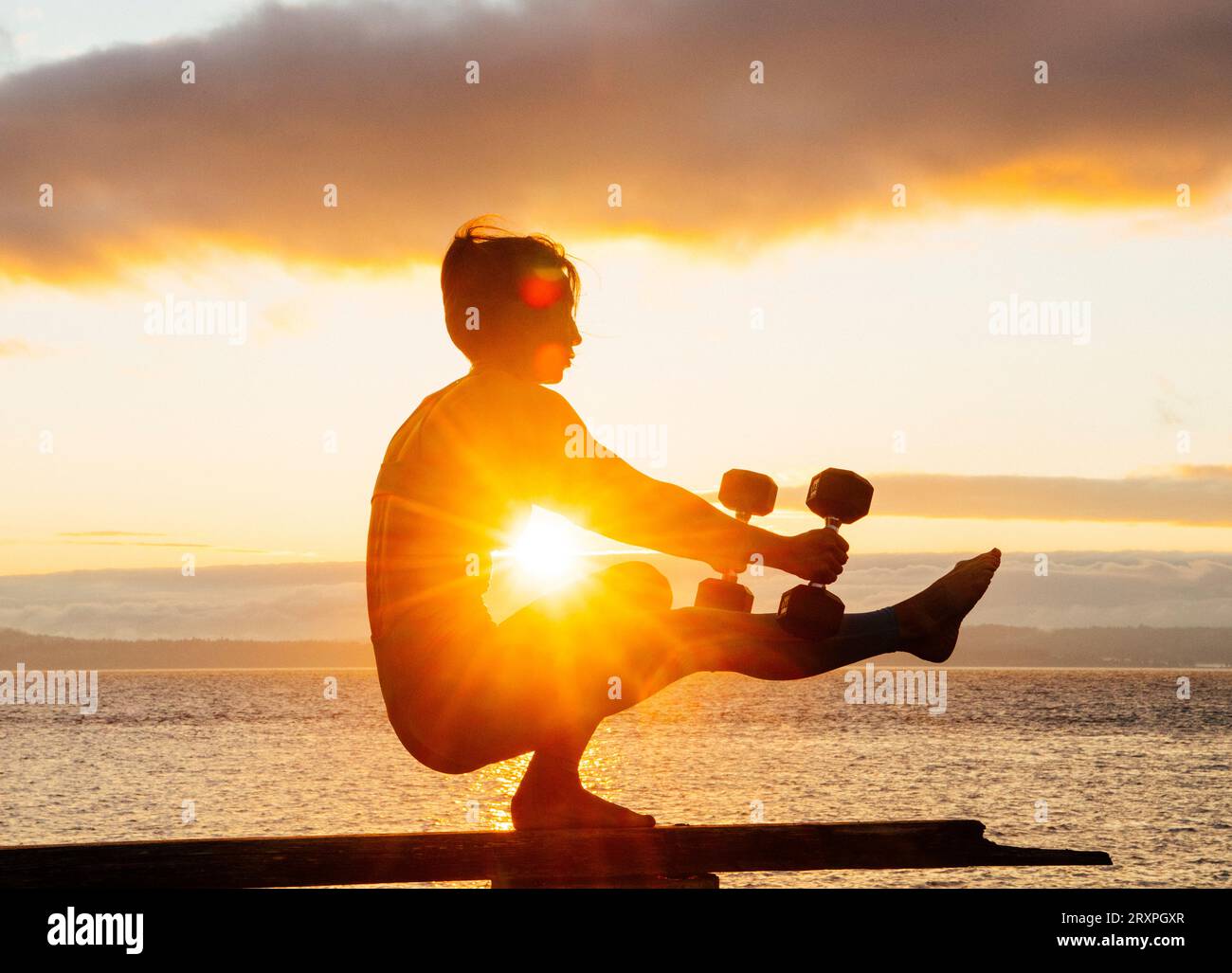 Silhouette de femme s'exerçant avec des haltères sur le dessus du banc côtier au crépuscule nuageux Banque D'Images