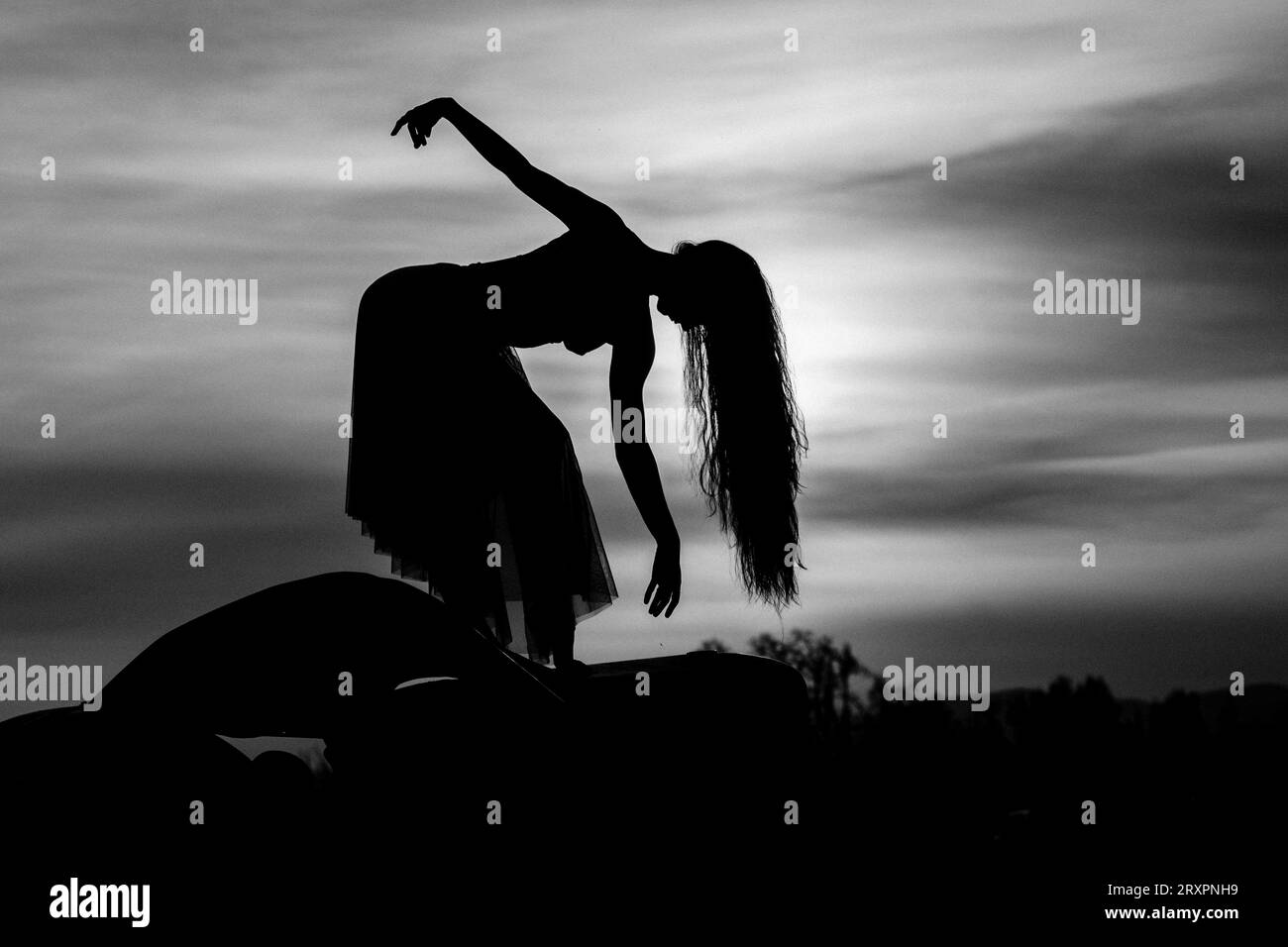 Silhouette de femme aux cheveux longs posant contre le soleil couchant Banque D'Images