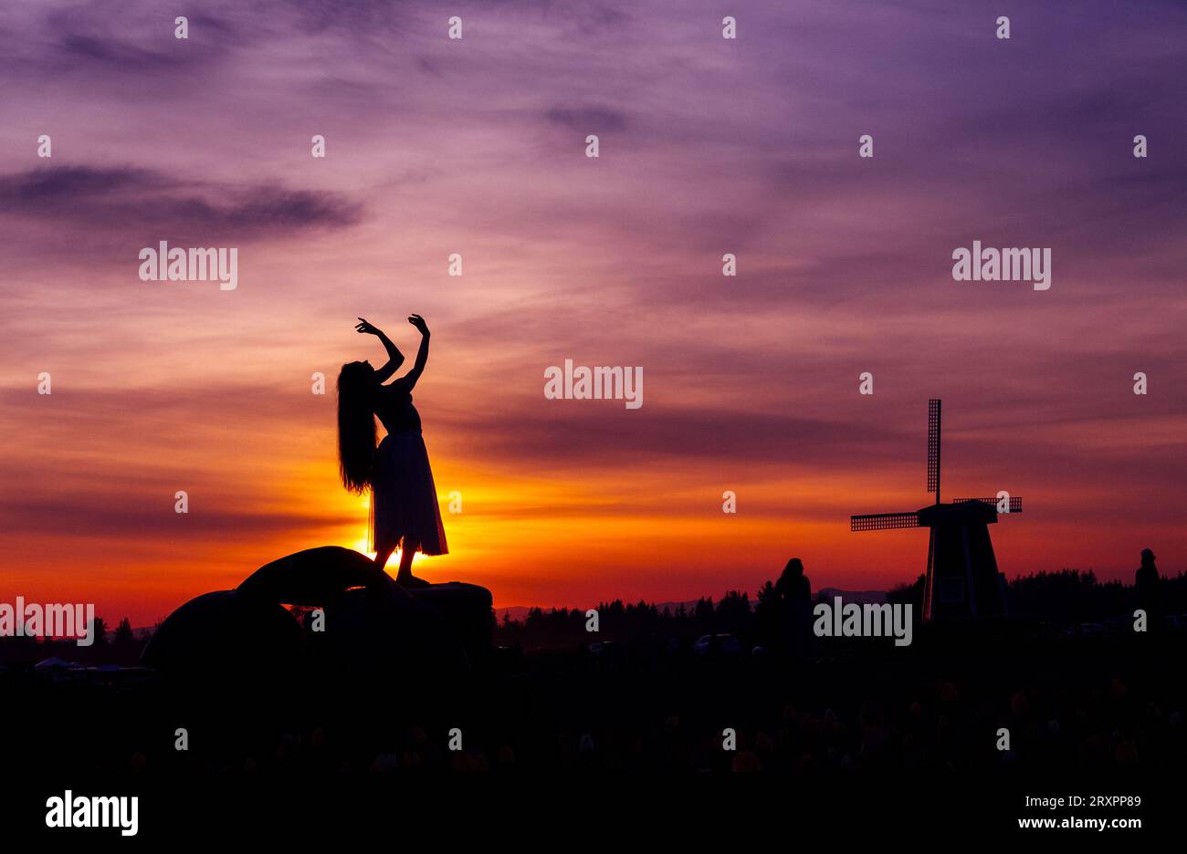 Silhouette de femme aux cheveux longs posant contre le soleil couchant avec moulin à vent en arrière-plan Banque D'Images