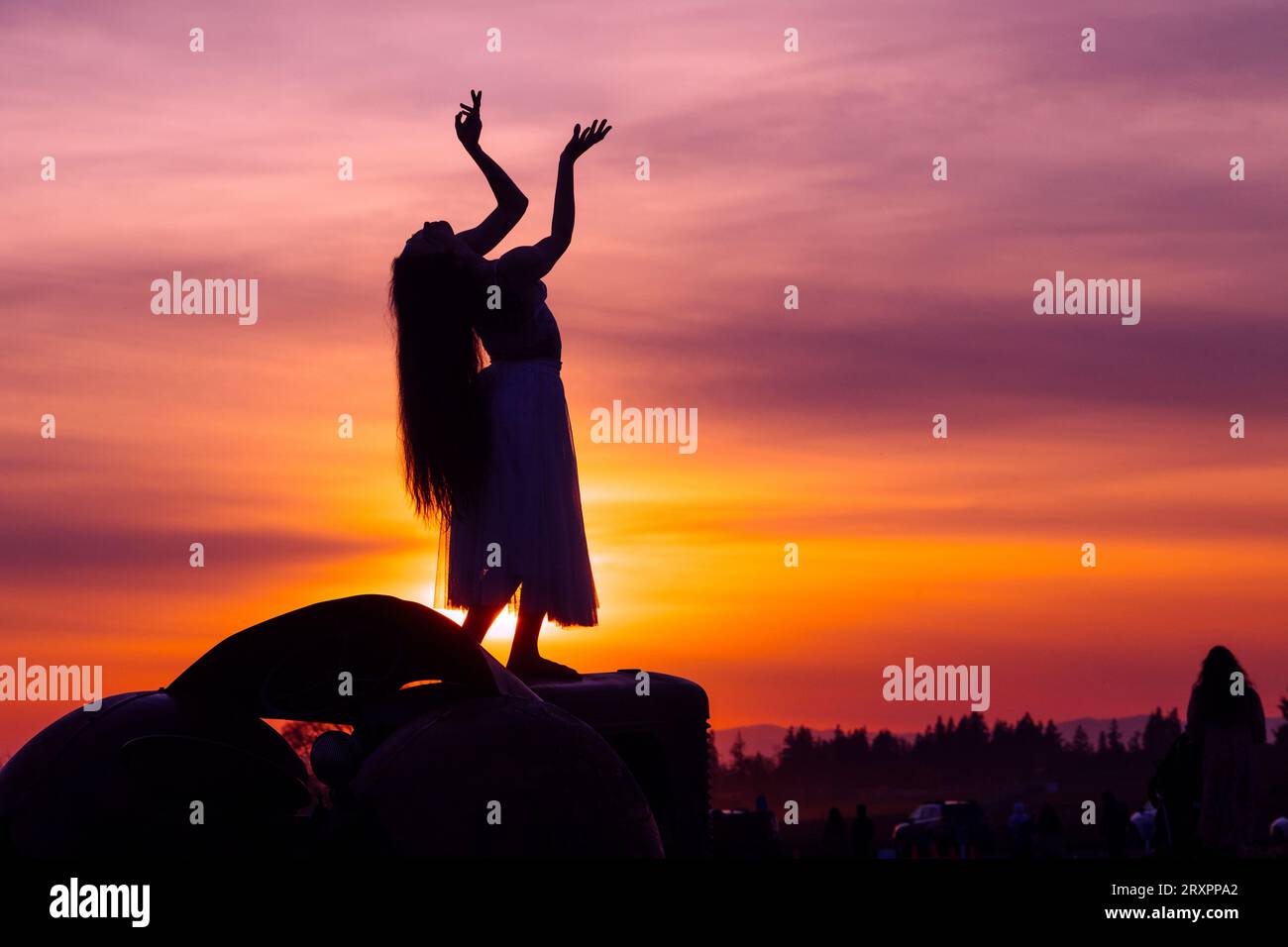 Silhouette de femme aux cheveux longs posant contre le soleil couchant avec moulin à vent en arrière-plan Banque D'Images