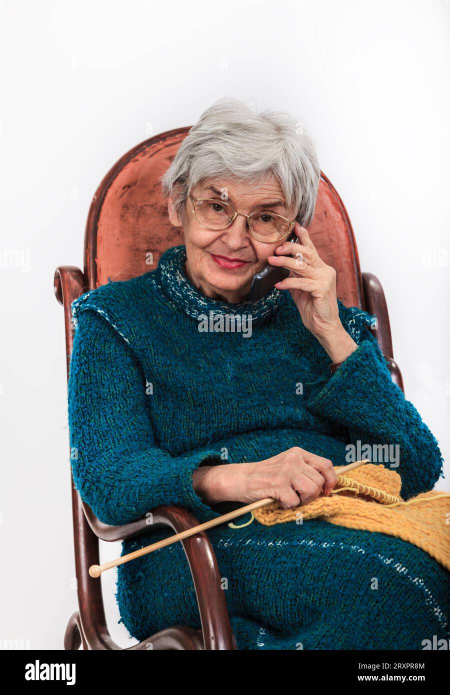 Portrait d'une femme âgée sur le mobile tout en étant assise dans un rocker tricotage. Banque D'Images