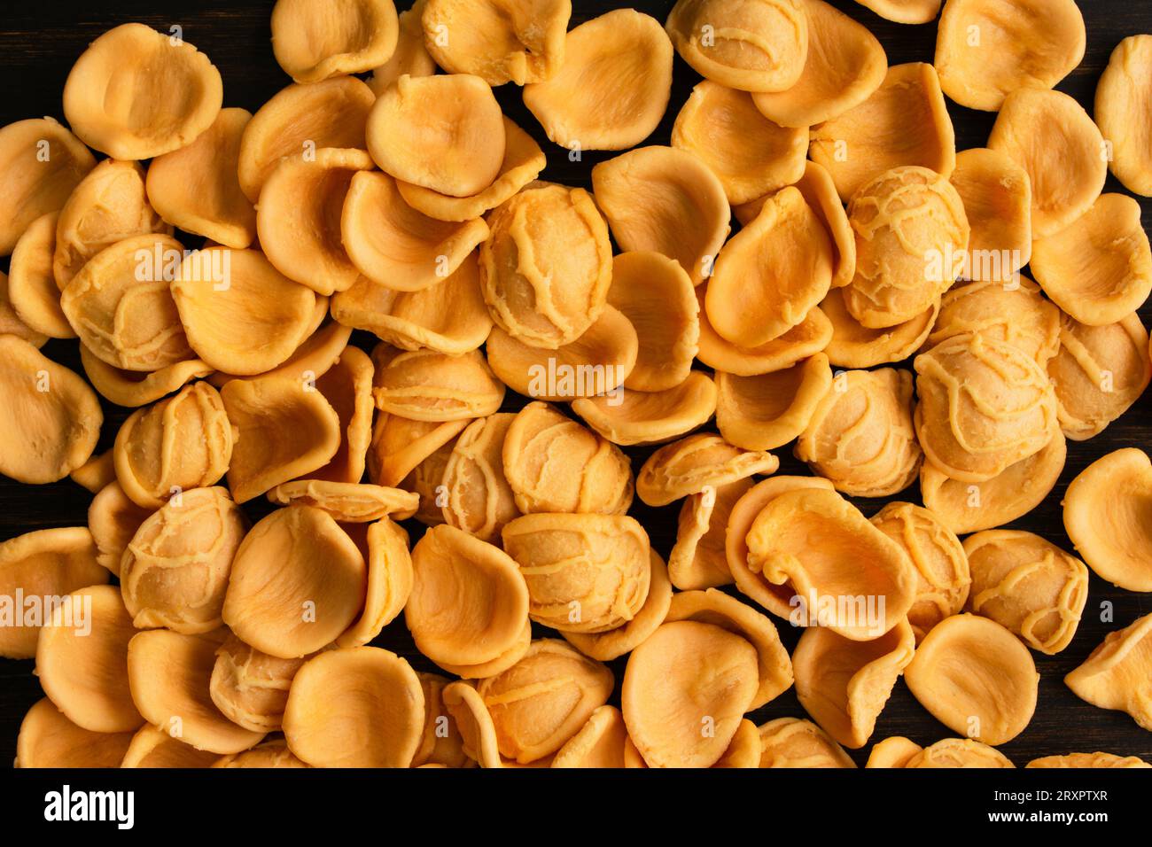 Pâtes orecchiette séchées orecchiette scattered sur une table en bois : morceaux de pâtes orecchiette non cuites sur un fond de bois sombre Banque D'Images