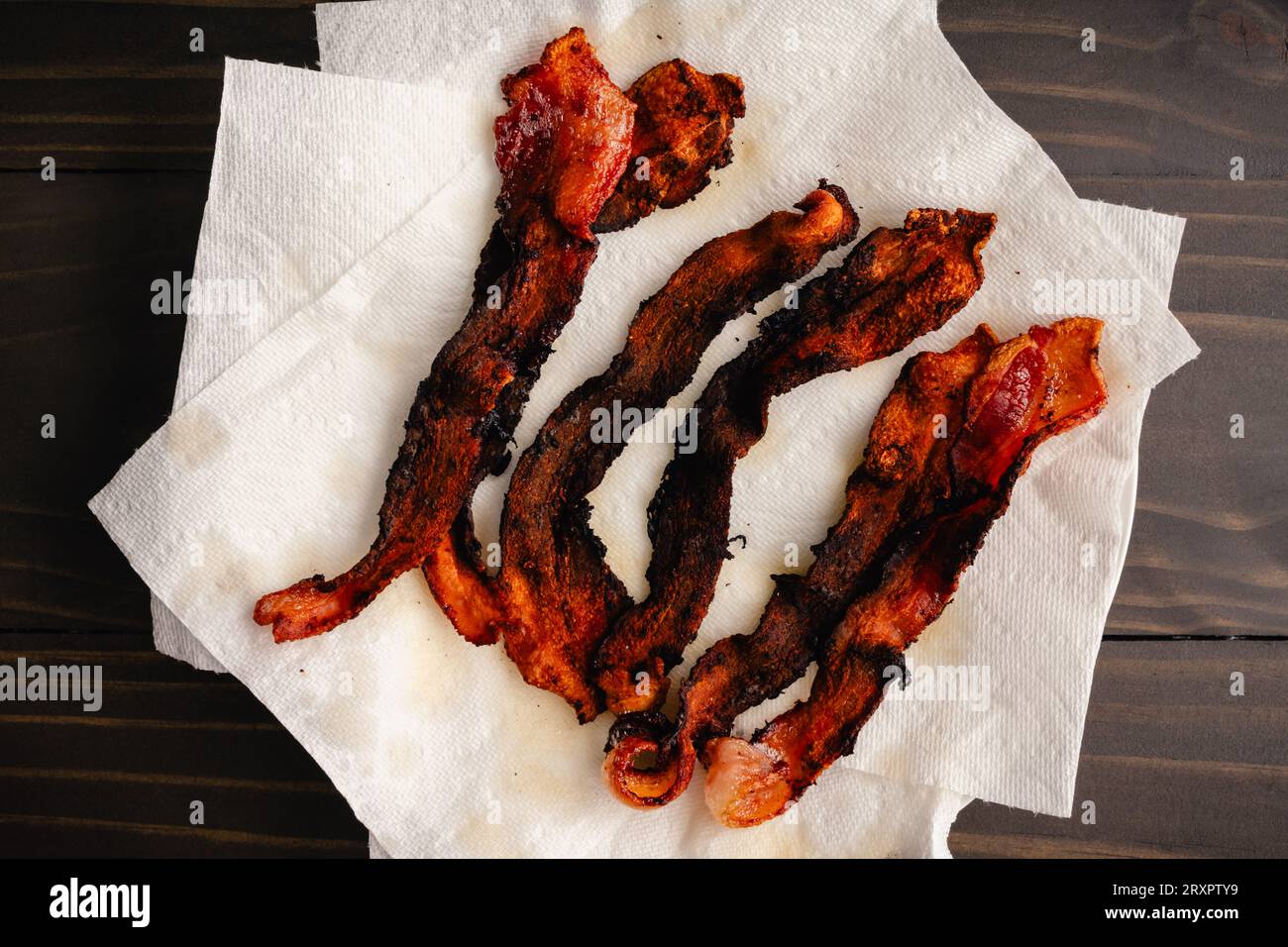 Bacon trop cuit égouttant sur des essuie-tout : tranches de bacon épais brûlé et strié égouttant sur du papier absorbant Banque D'Images