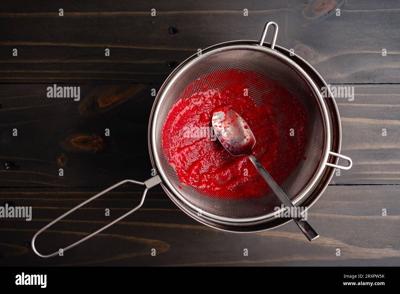 Filtrer la purée de fraises avec une crépine en maille : faire de la purée de fraises avec un petit bol de graines sur le côté Banque D'Images