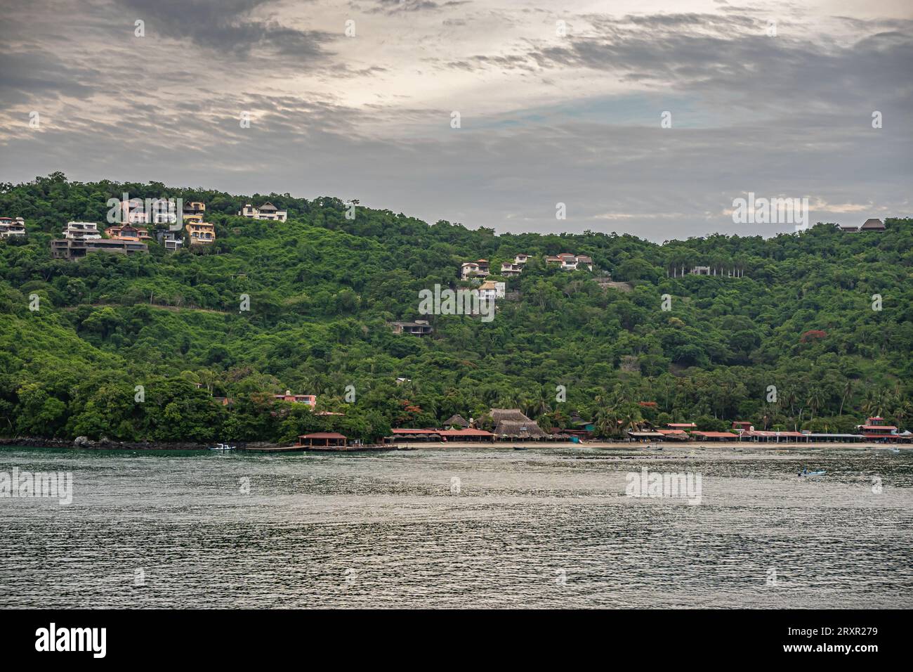 Zihuatanejo, Mexique - 18 juillet 2023 : toits rouges de la station le long de la plage de sable de East Side Bay. Collines boisées vertes avec demeures dispersées et condominium Banque D'Images