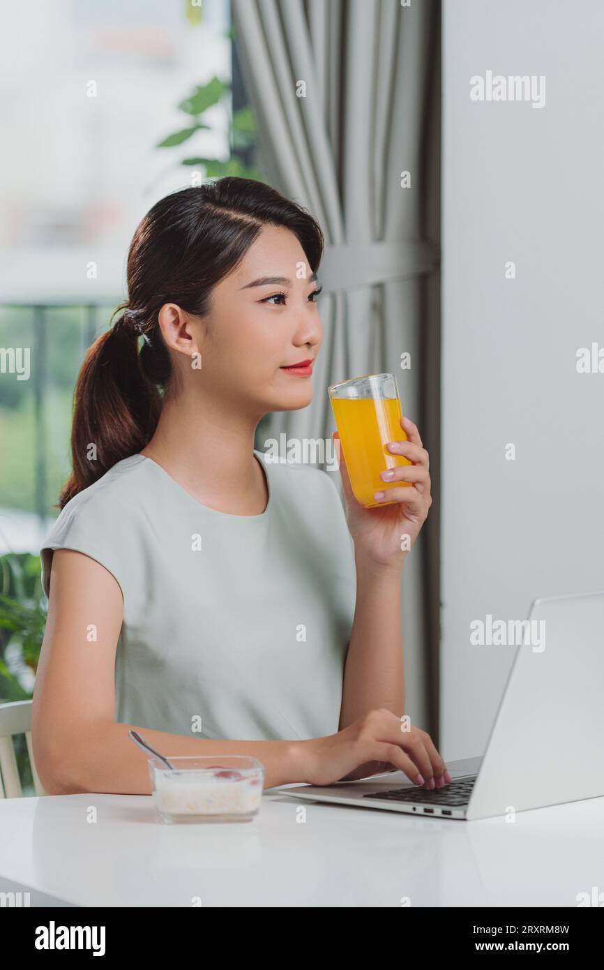 Femme satisfaite buvant du jus d'orange à l'aide d'un ordinateur portable sur un bureau à la maison Banque D'Images