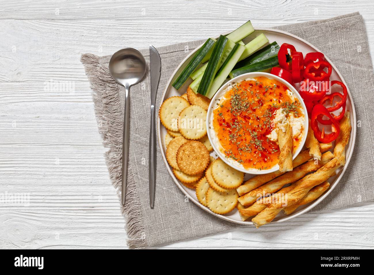 Trempette au fromage gelé au poivre chaud dans un bol servi avec des craquelins, des gressins italiens croustillants, du poivre frais et du concombre sur un plateau en bois blanc, à l'horizontale Banque D'Images