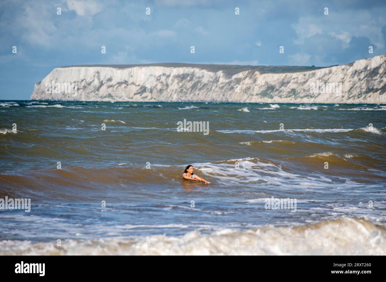 femme nageant dans la mer dans de grandes vagues brisantes sur une journée venteuse ou venteuse à compton bay sur l'île de wight avec des falaises en arrière-plan Banque D'Images