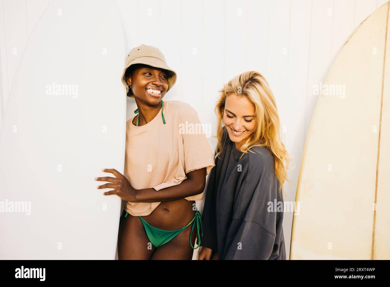 Portrait de deux jeunes femmes joyeuses debout avec leurs planches de surf après une journée de repos à la plage. Deux surfeuses en maillot de bain tenant leur surfboa Banque D'Images