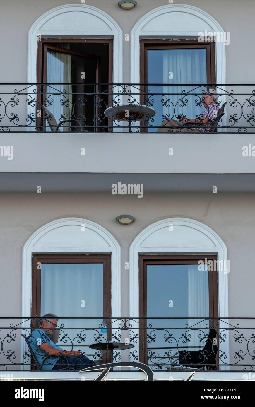 remorquez des hommes plus âgés assis sur leur balcon seuls à différents niveaux d'un immeuble d'appartements ou de chambres d'hôtel Banque D'Images