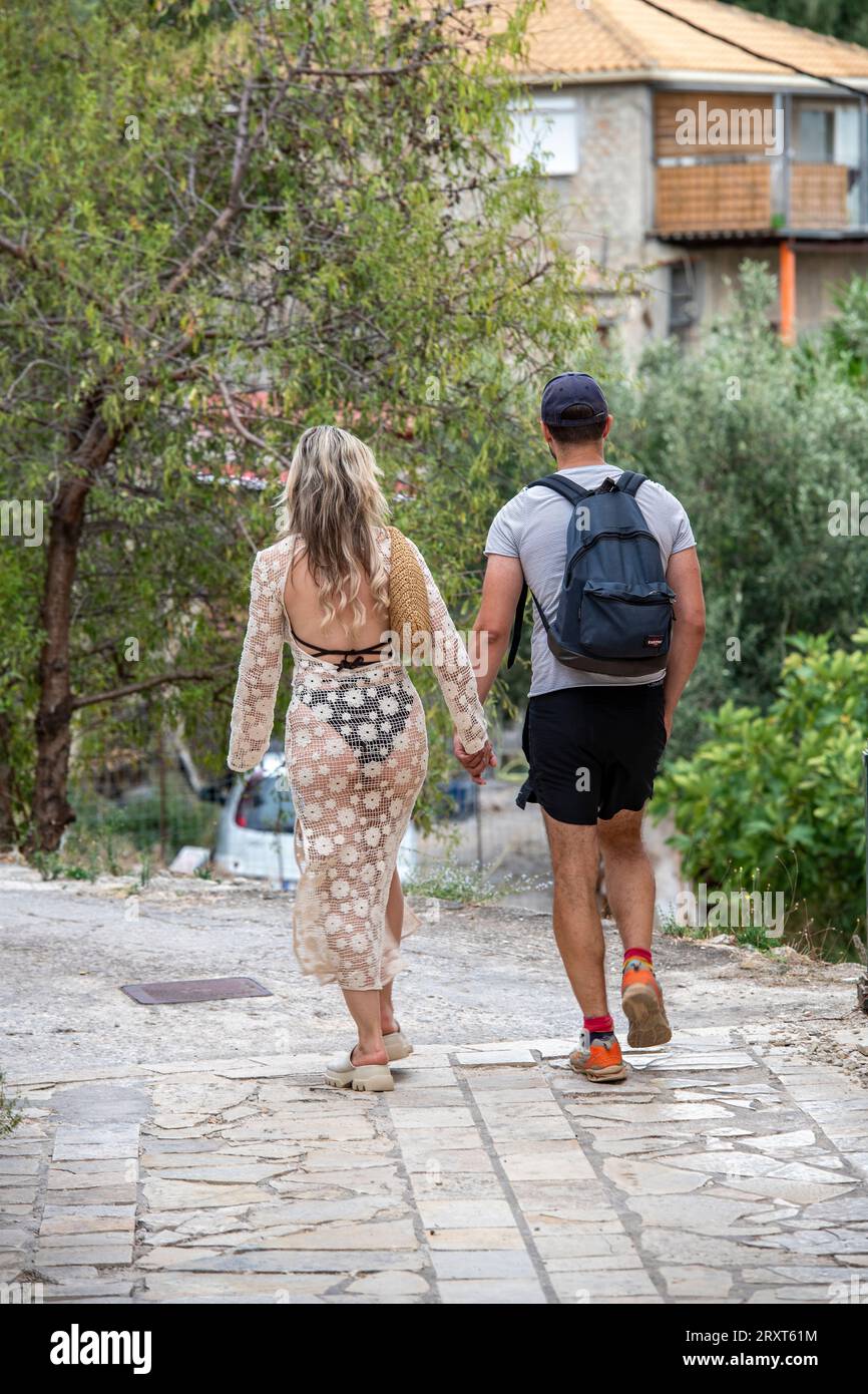 jeune couple marchant main dans la main en vacances sur l'île de zante ou zakynthos avec une dame portant une robe transparente avec des vêtements révélateurs. Banque D'Images