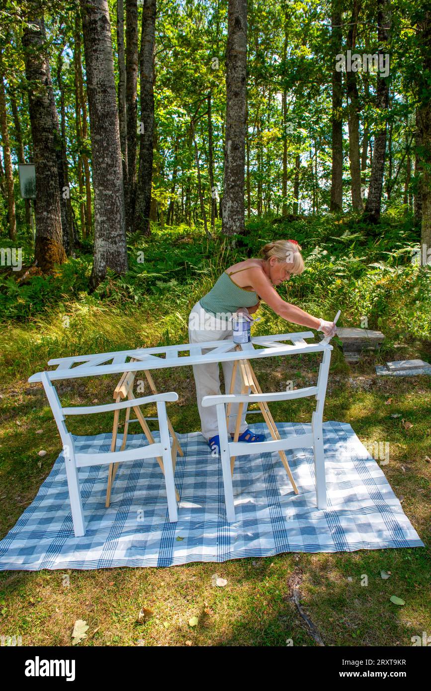 Une femme âgée peignant un meuble d'extérieur Banque D'Images