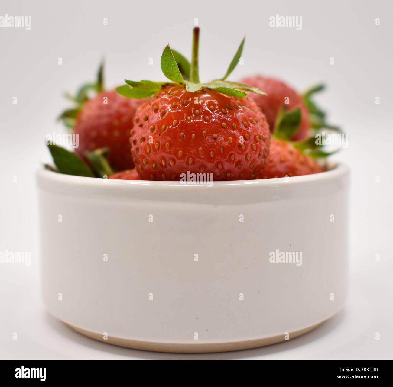 Un petit bol blanc contenant des fraises rouges juteuses photographiées sur fond blanc. Banque D'Images