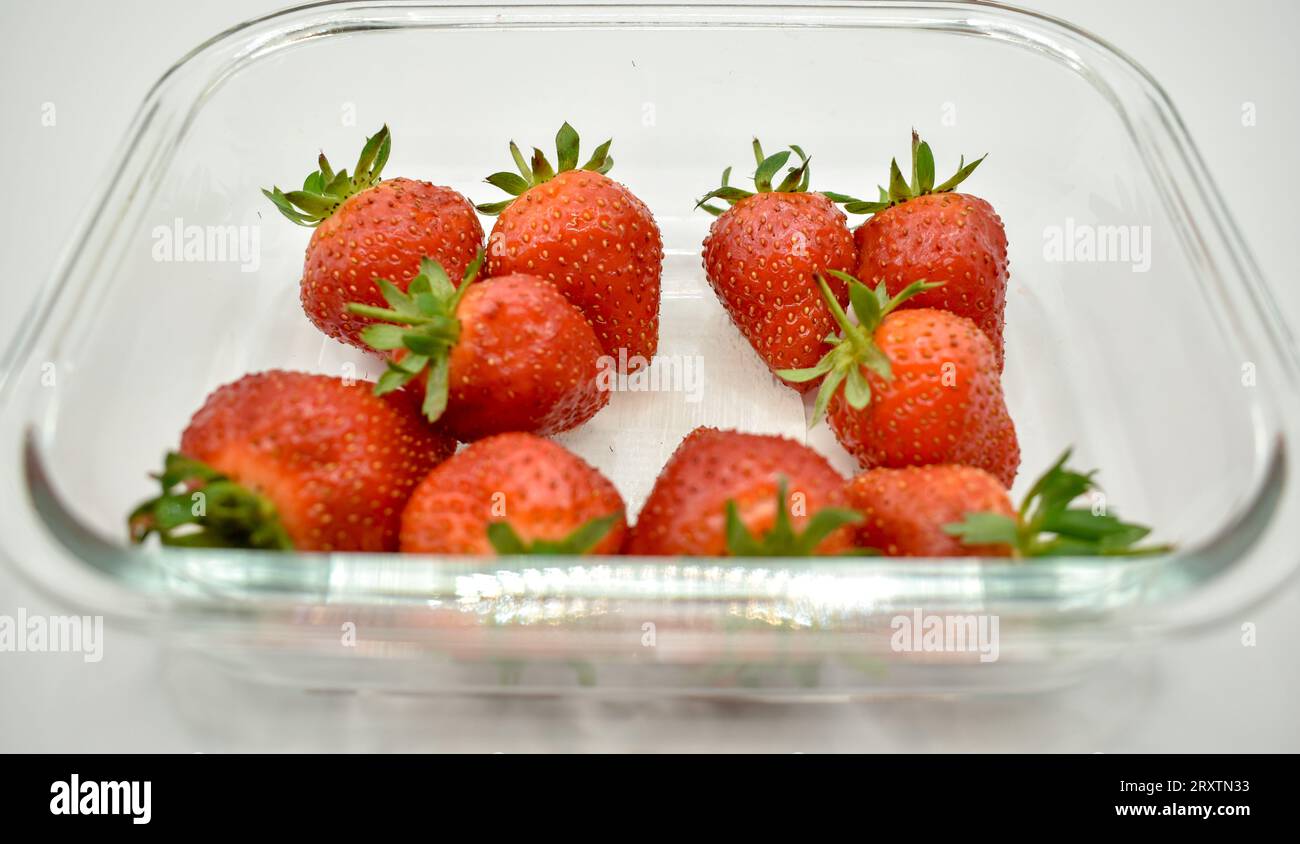 Un plat en verre transparent contenant des fraises rouges juteuses photographiées sur fond blanc. Banque D'Images